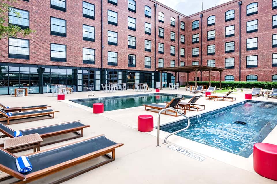 Resort pool courtyard with lounge chairs, pink accents, and red brick architecture