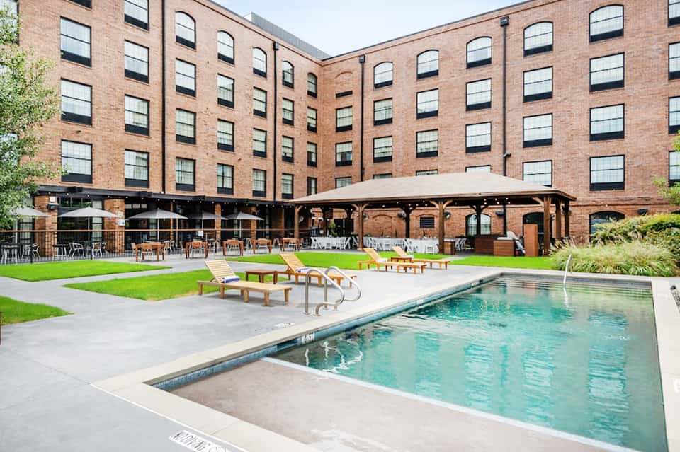 Hotel courtyard with brick building, covered pavilion, pool, lounge chairs, and manicured lawn