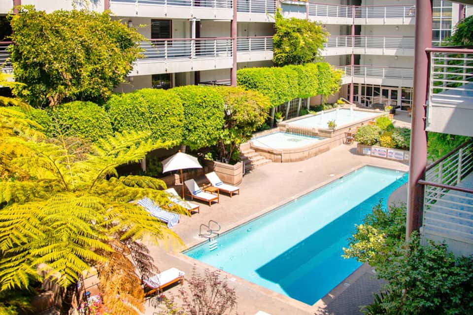 Aerial view of hotel courtyard with rectangular pool, lush green landscaping, and lounge area
