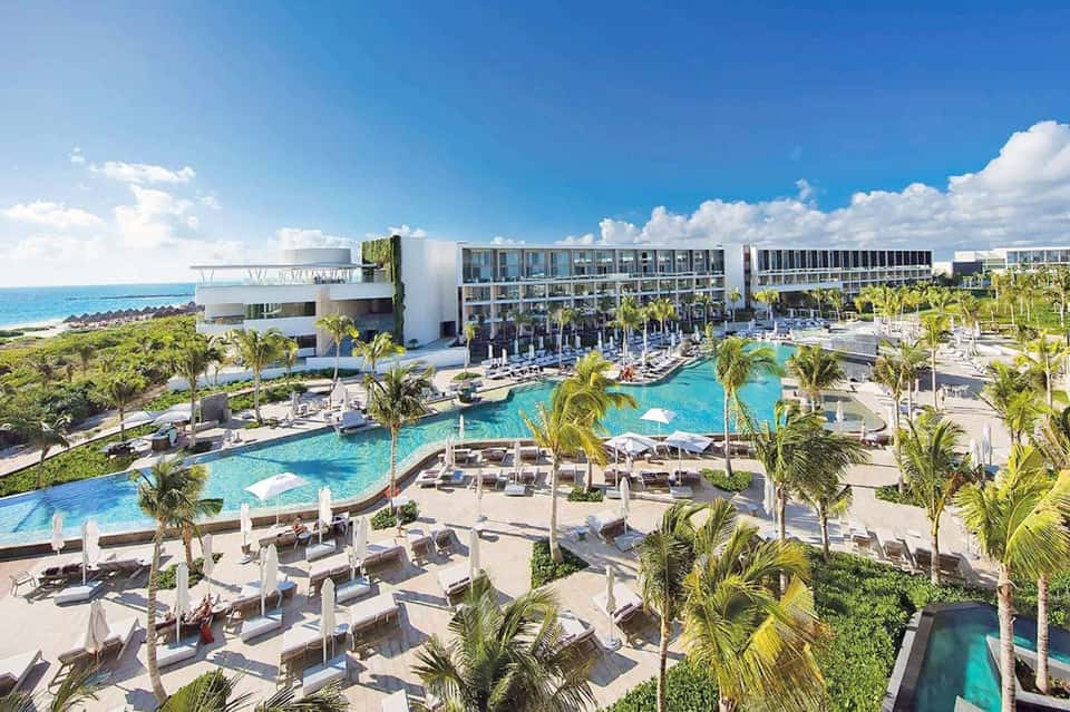 Aerial view of modern beachfront resort with turquoise pools, palm trees, and ocean