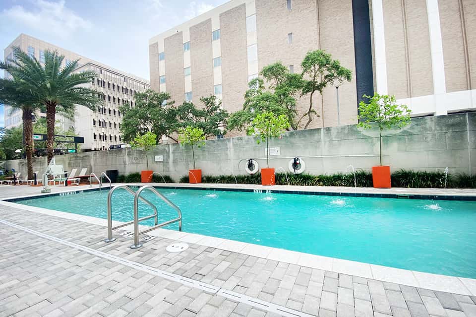 Resort swimming pool with lounge chairs and modern building with orange accent walls and palm trees