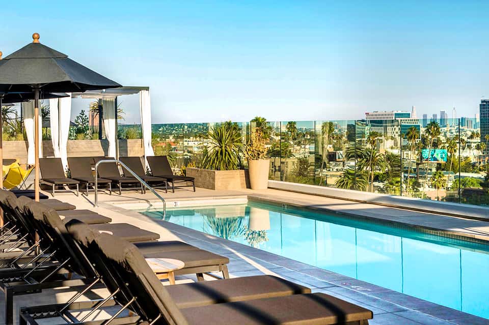 Rooftop infinity pool with lounge chairs and cabanas overlooking palm trees and city skyline