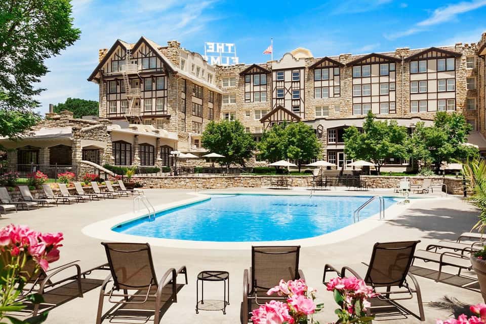Historic stone resort building with pool surrounded by lounge chairs, umbrellas, and manicured landscaping