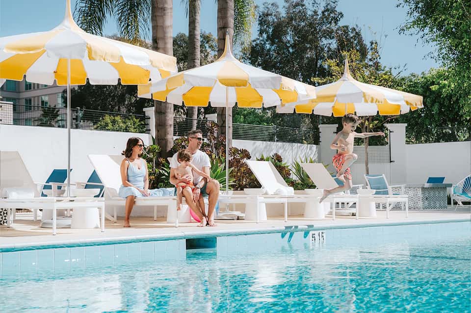 Family relaxing by resort pool under yellow and white striped umbrellas with lounge chairs