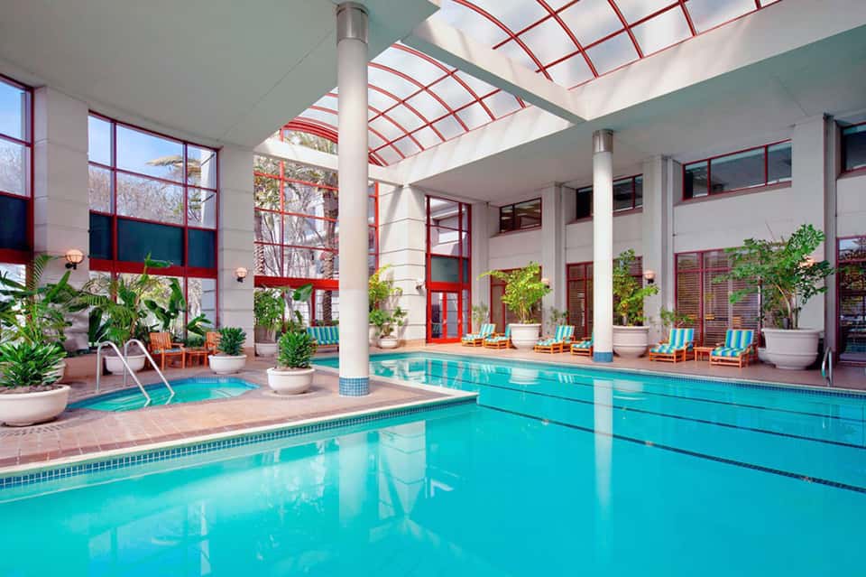 Indoor lap pool with red-trimmed skylights, potted plants, and lounge seating