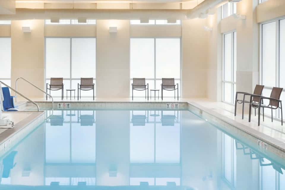 Bright indoor swimming pool with floor-to-ceiling windows and lounge chairs in a luxury hotel