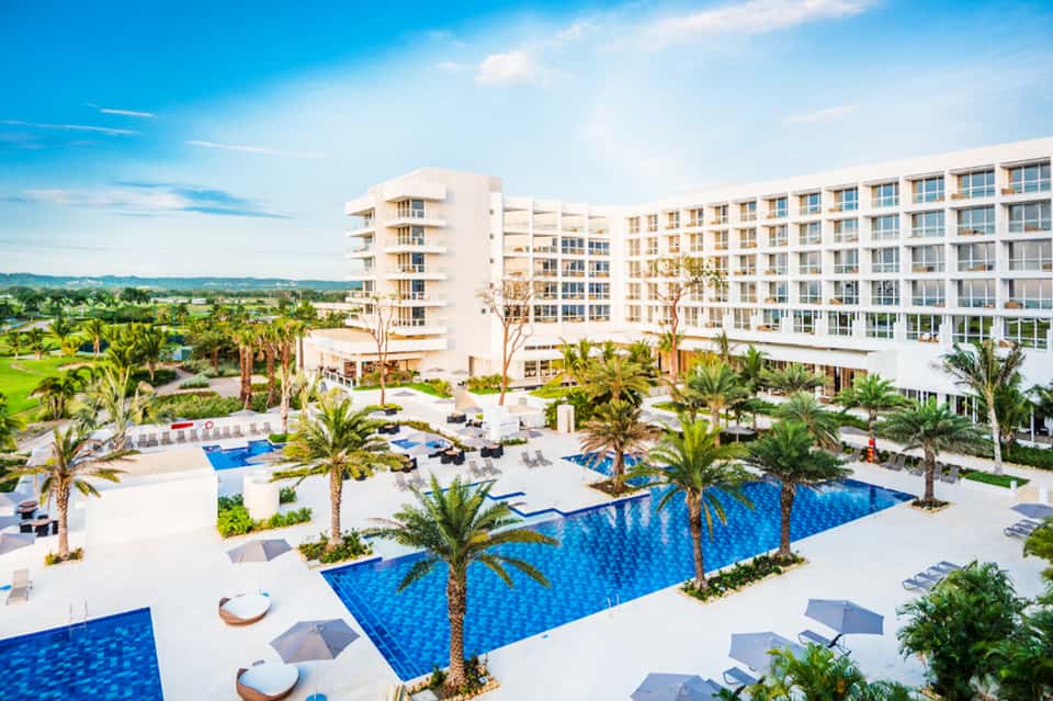 Aerial view of beachfront resort with blue pools, palm trees, and modern architecture