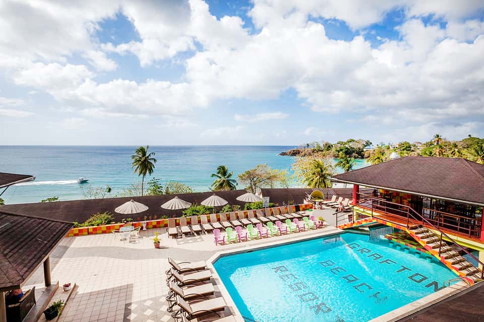 Aerial view of resort pool deck with blue swimming pool, lounge chairs, umbrellas, and ocean views with palm trees