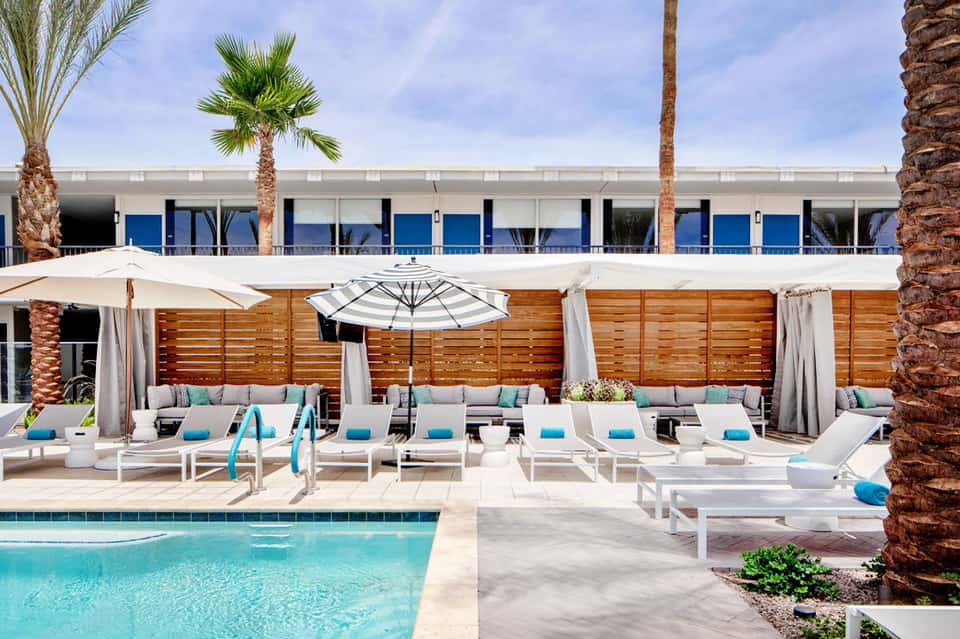 Resort pool deck with white lounge chairs, umbrellas, and wooden privacy screens overlooking turquoise water