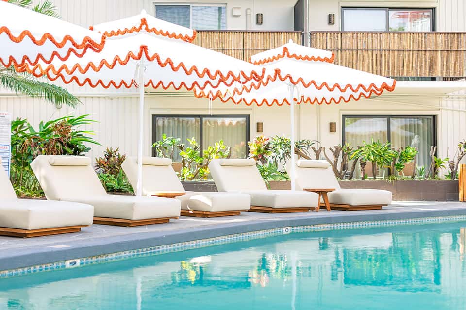 Poolside lounge area with white cushioned sun loungers under white and orange wave-patterned shade