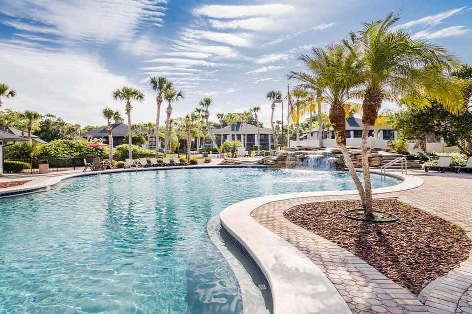 Luxurious resort pool with palm trees, lounge chairs, and elegant pool houses in background