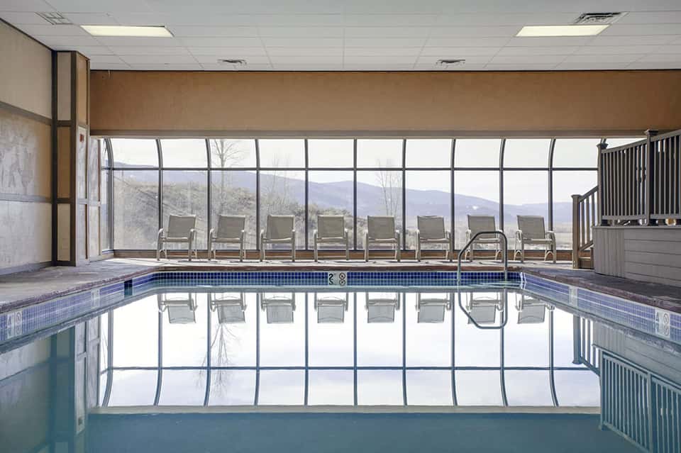 Indoor lap pool with large windows overlooking mountains and lounge chairs along the deck
