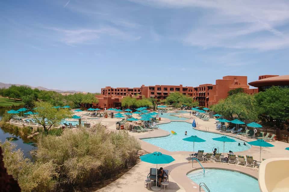 Large resort pool complex with turquoise umbrellas, red architecture, and desert landscape