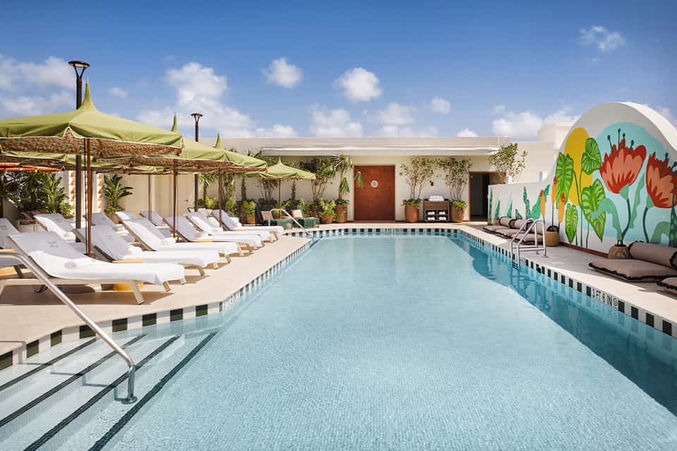 Resort pool with yellow umbrellas, lounge chairs, colorful mural wall, and clear sky