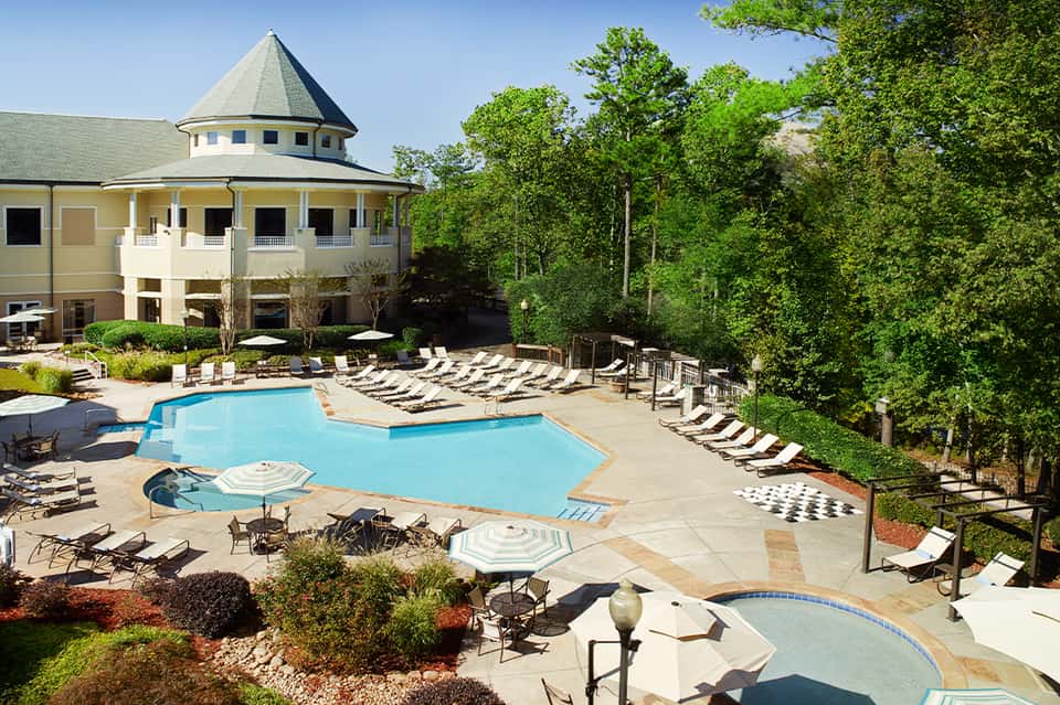 Resort pool with tower building, lounge chairs, and lush forest surroundings