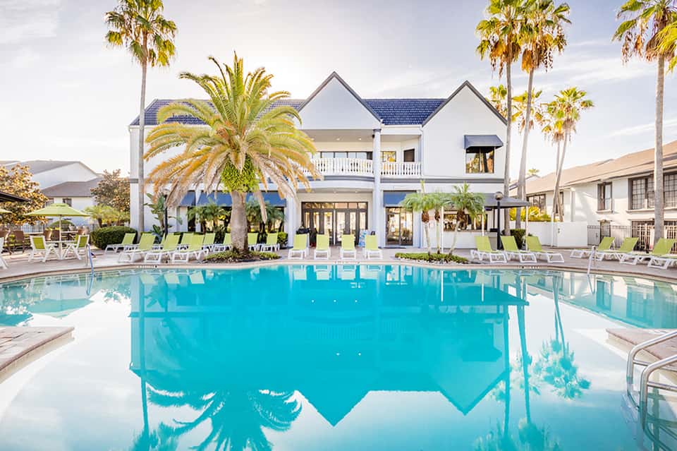 Beachfront resort pool with white house, palm trees, and loungers