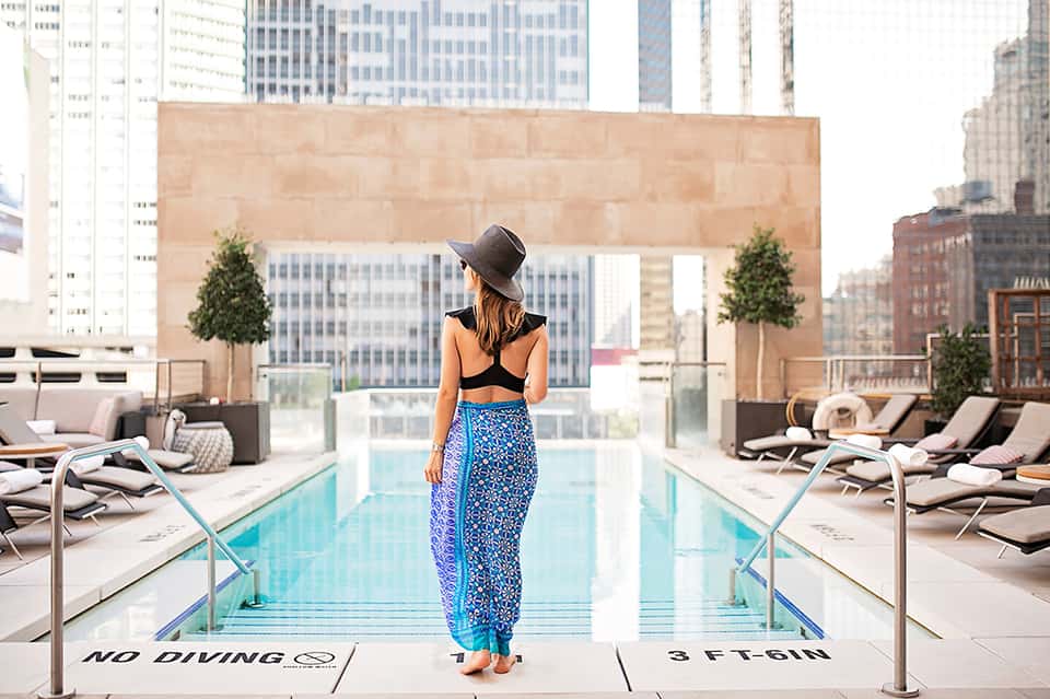 Woman at edge of rooftop pool overlooking urban skyline with downtown buildings