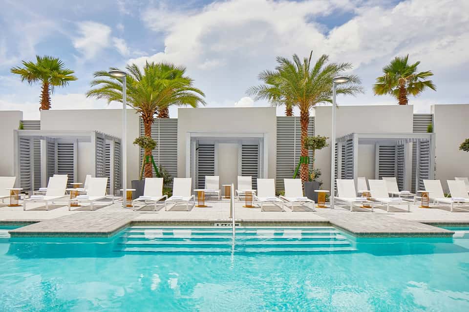 Contemporary pool deck with white loungers, palm trees, white cabanas, and turquoise water