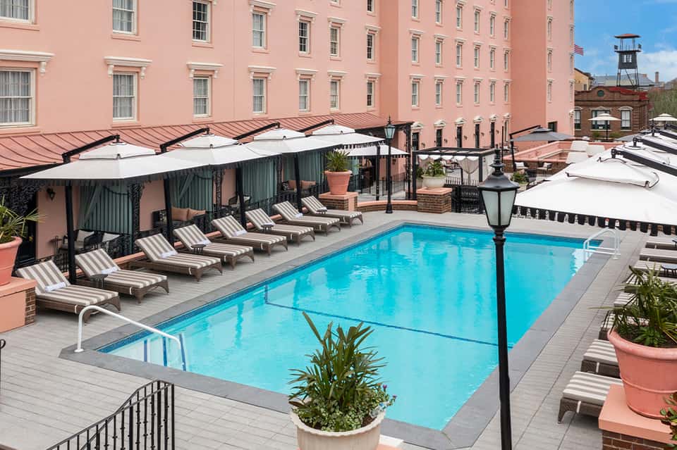 Rooftop pool at pink hotel building with white umbrellas, lounge chairs and historic brick architecture backdrop