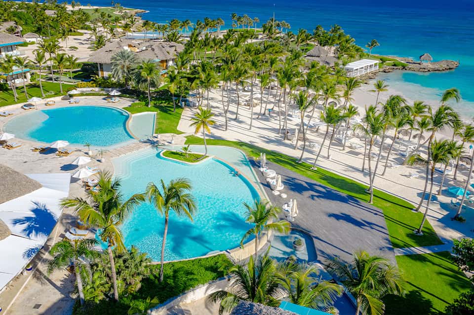 Aerial view of resort with multiple pools, palm trees, and ocean