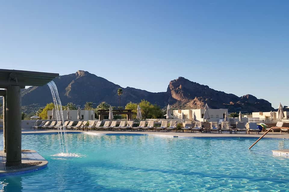 Resort pool with mountain backdrop, white lounge chairs, and cabanas in desert setting