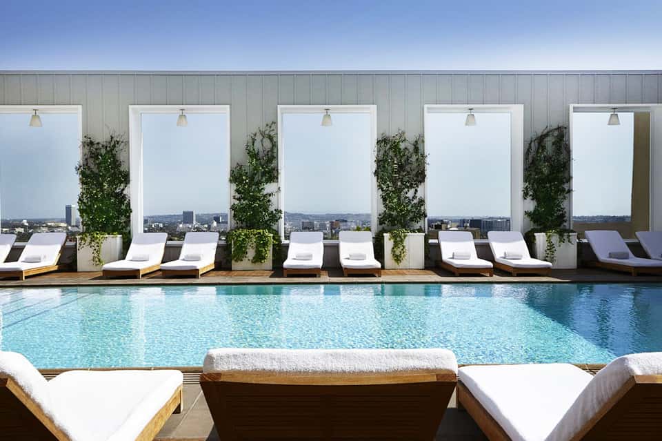 Rooftop pool with city skyline view, white lounge chairs, large white privacy screens, and landscaping