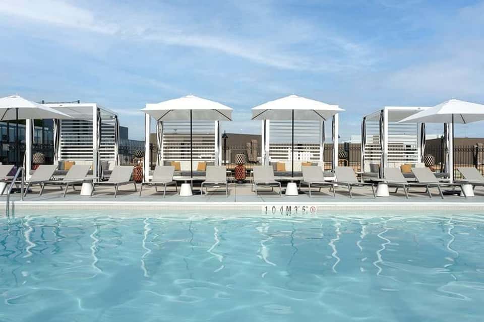 Rooftop pool with white cabanas, umbrellas, lounge chairs, and ocean backdrop