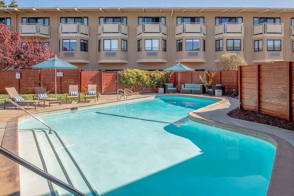 Resort pool with turquoise water, lounge chairs, red wooden privacy fences, and multi-story hotel building