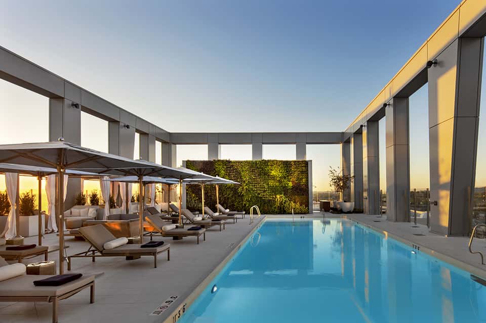 Indoor luxury pool with glass walls, lounge chairs with cabanas, and city skyline at sunset