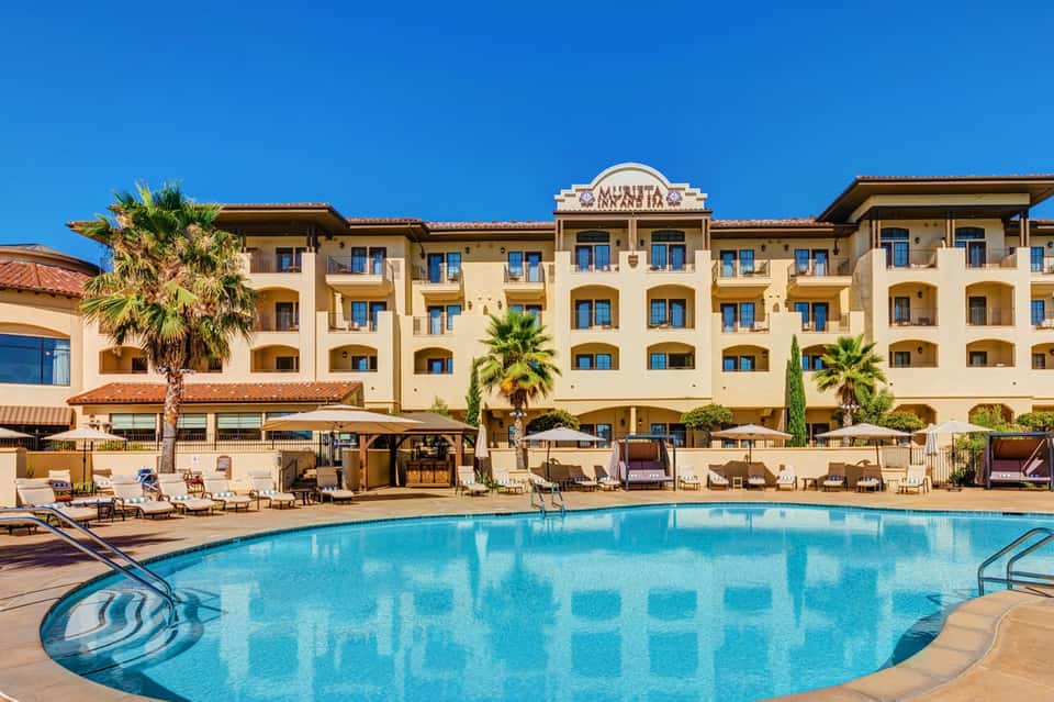 Spanish-style resort exterior with palm trees, terracotta roof, and large swimming pool with loungers
