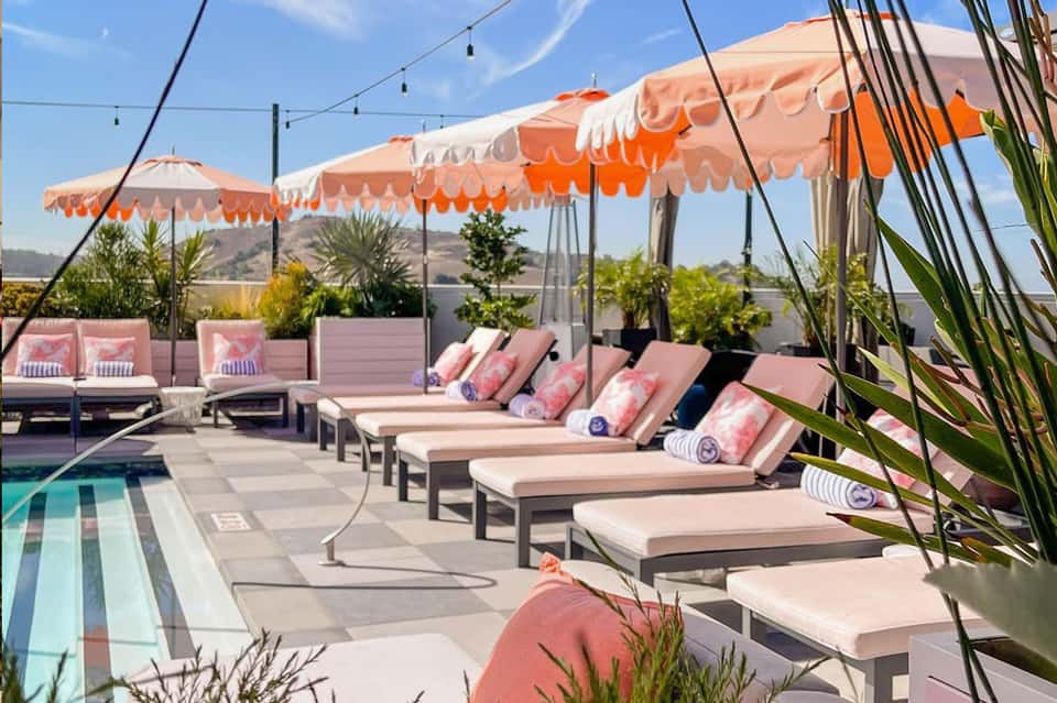 Chic rooftop pool deck with pink and white umbrellas, lounge chairs, and mountain views