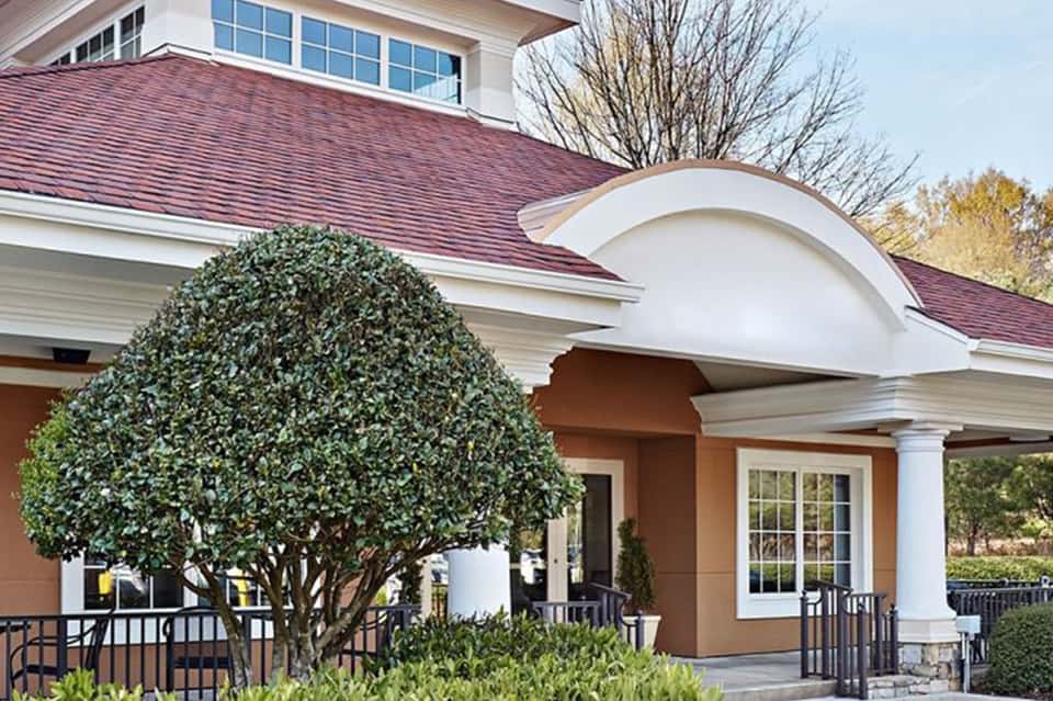 Elegant colonial-style building entrance with burgundy roof, white columns, and manicured landscaping