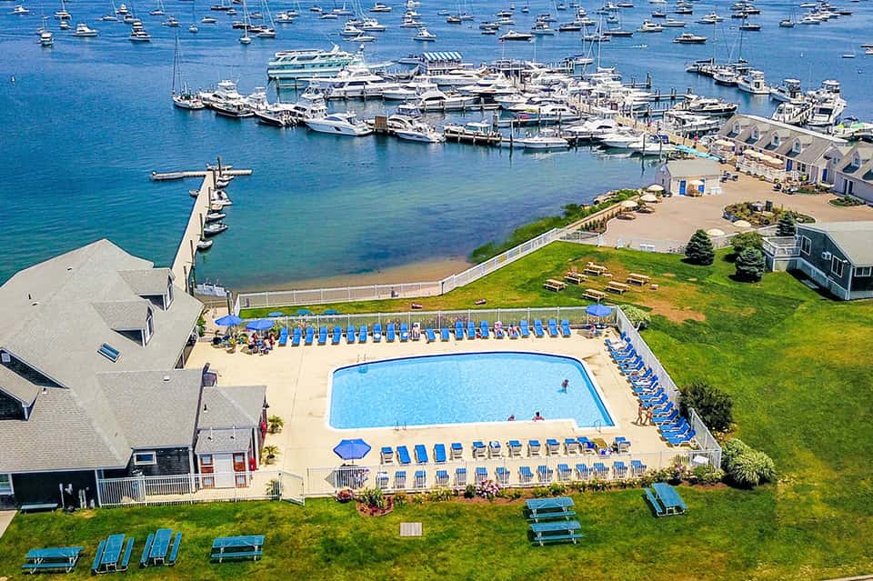 Waterfront resort pool overlooking marina with boats, beach, green lawn, and blue beach umbrellas
