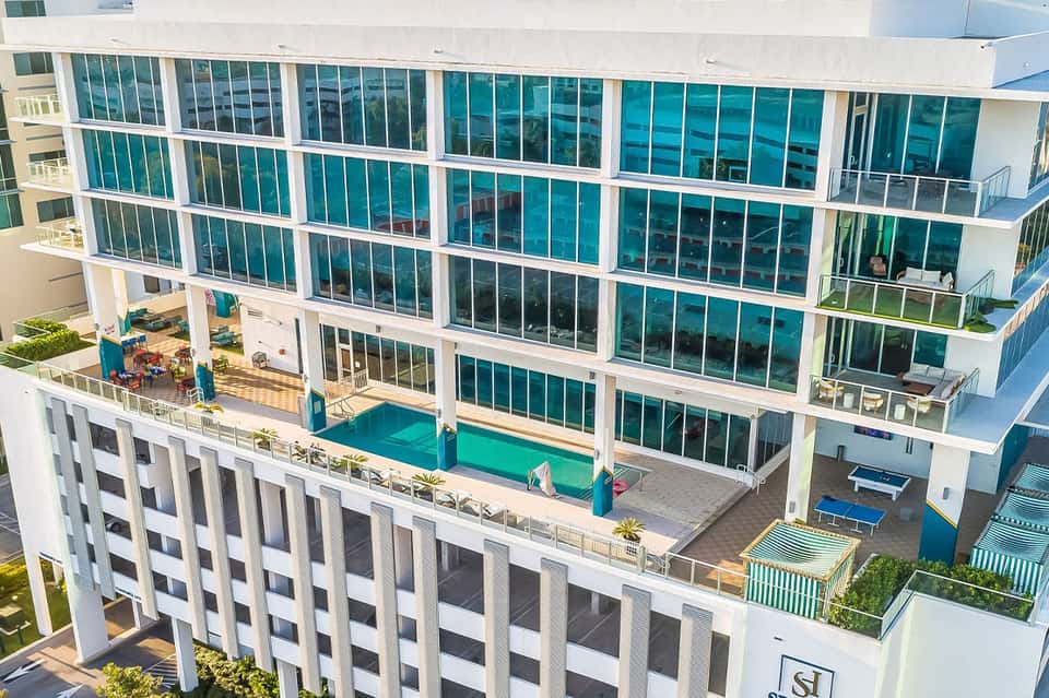 Modern oceanfront resort building with teal-green windows, white frame, ground-level pool, and multiple balconies
