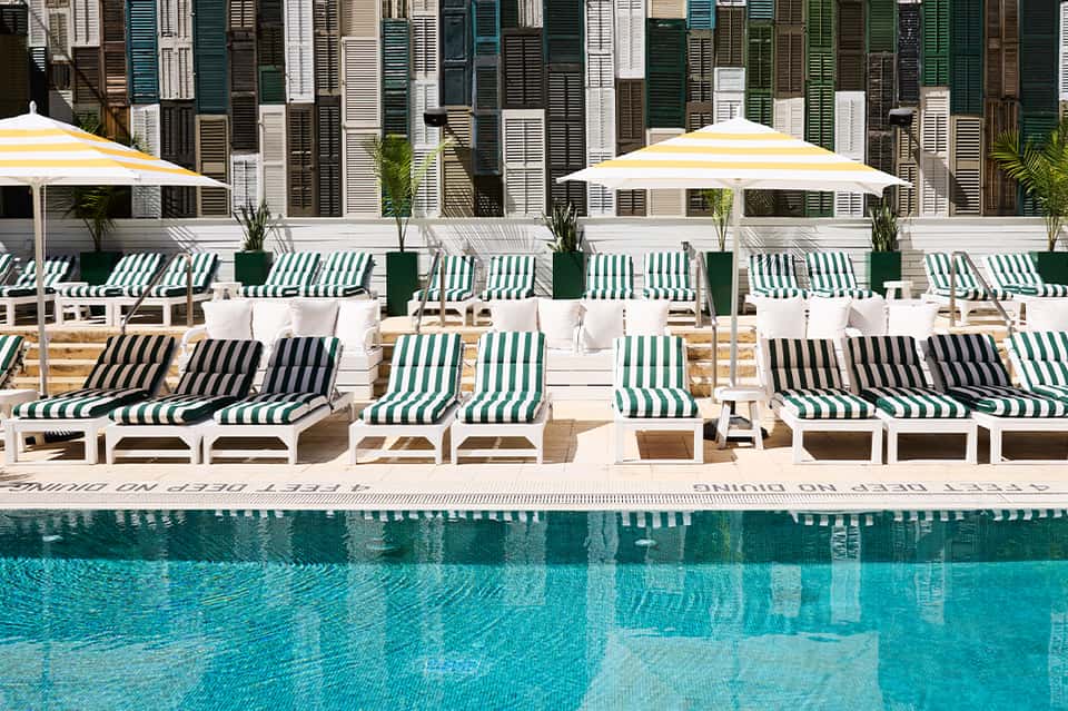 Resort pool deck with striped lounge chairs, yellow umbrellas, and colorful shuttered building backdrop