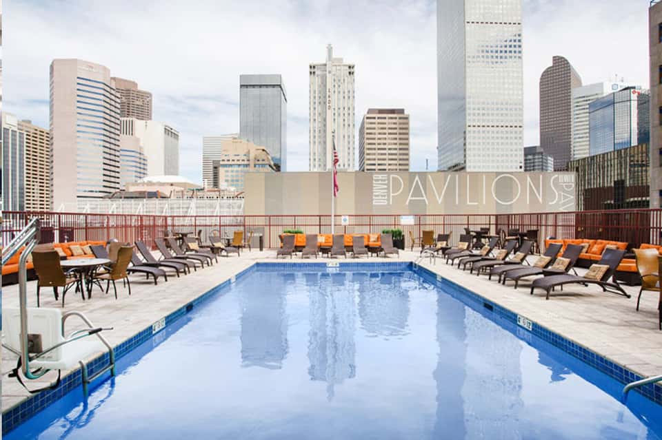 Urban rooftop pool at Pavilions with city skyline backdrop, loungers, and umbrellas