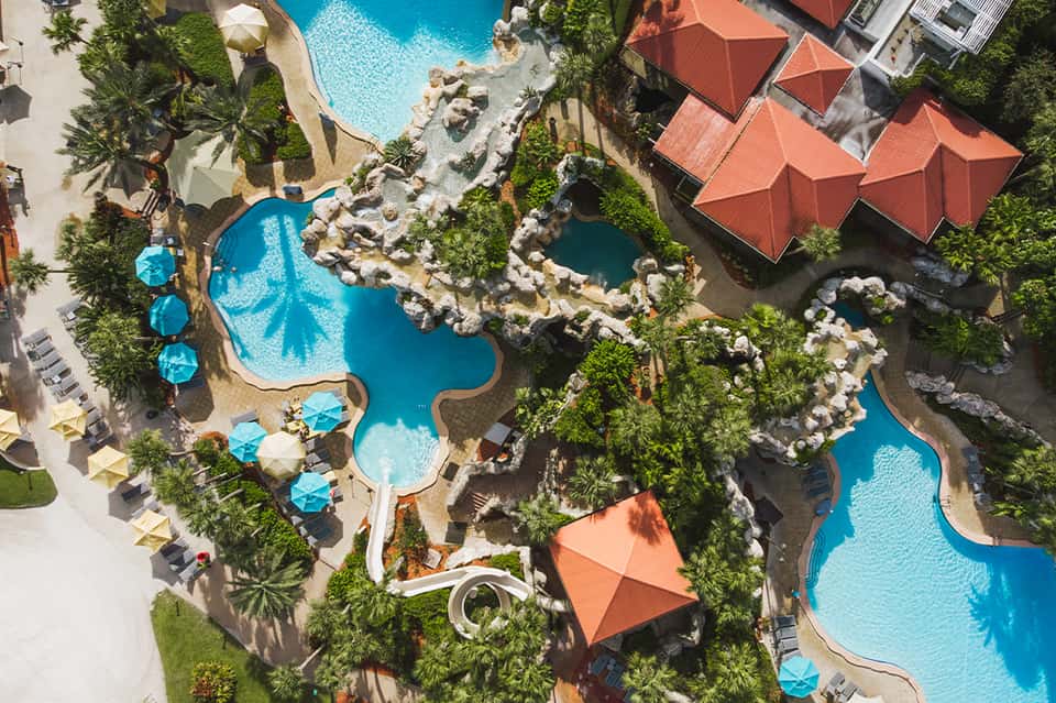 Aerial view of resort with multiple turquoise pools, tropical landscaping, orange umbrellas, and interconnected courtyards