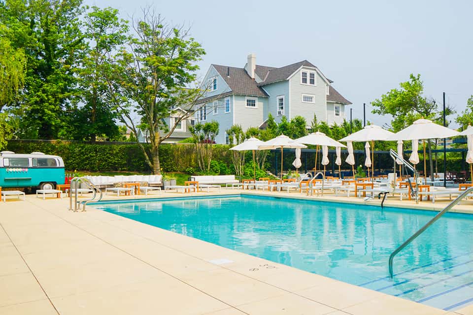 Rectangular lap pool with cream umbrellas, wooden lounge chairs, and farmhouse-style building
