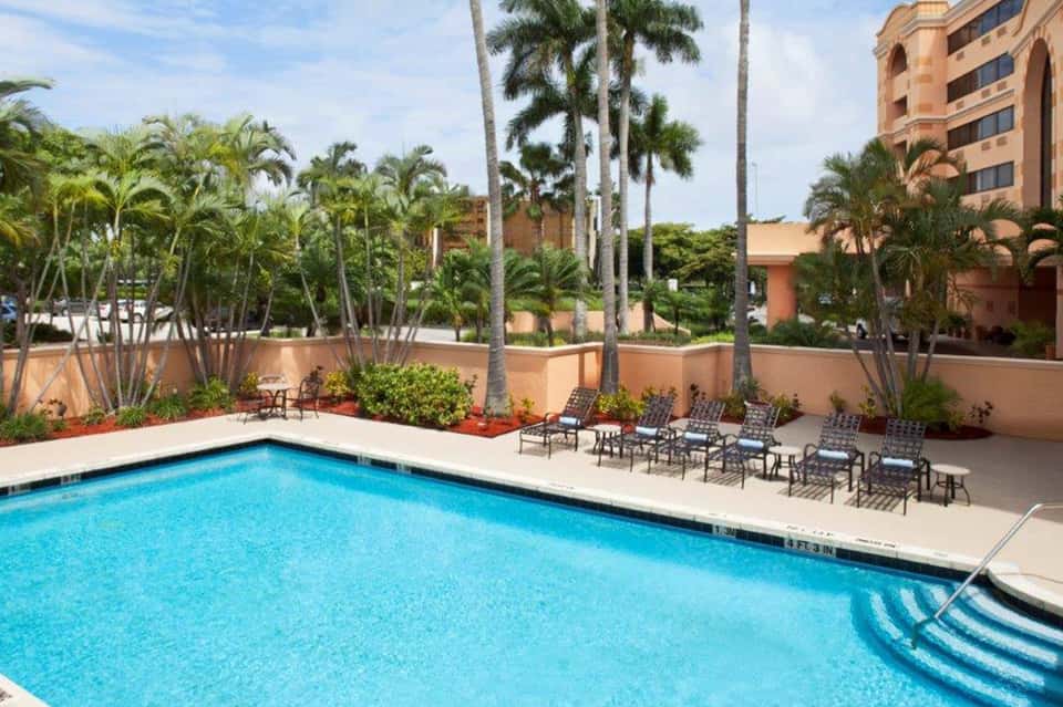 Resort pool surrounded by palm trees, lounge chairs, and terracotta buildings