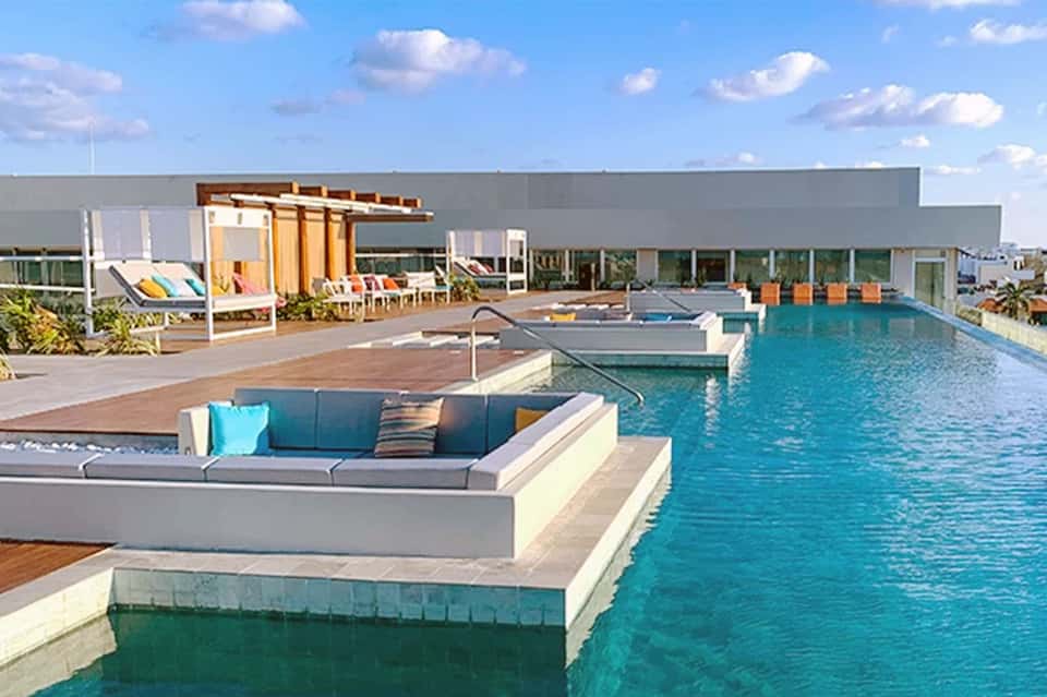 Modern rooftop pool with turquoise water, lounge seating, yellow pergola, and contemporary building