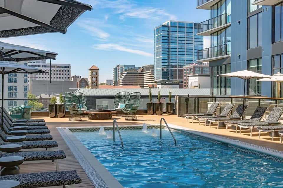 Urban rooftop pool deck with lounge chairs, umbrellas, and city skyline views