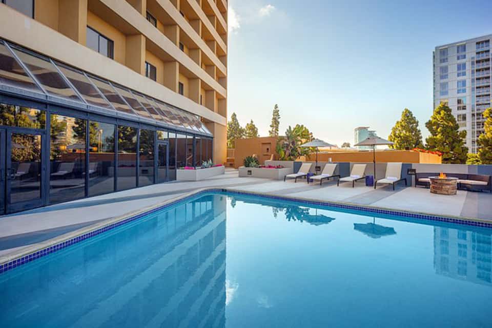 Contemporary rooftop pool with glass sliding doors, lounge chairs and city skyline visible at dusk