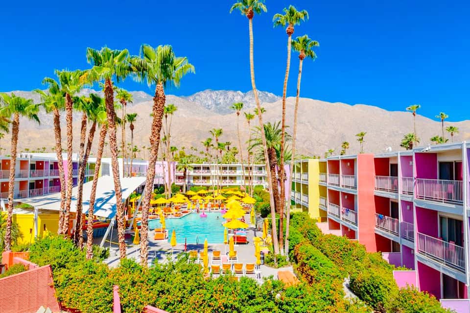 Colorful resort courtyard with bright buildings surrounding a turquoise pool and palm trees