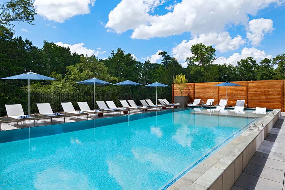 Luxury resort pool with white loungers, blue umbrellas, and manicured landscape backdrop