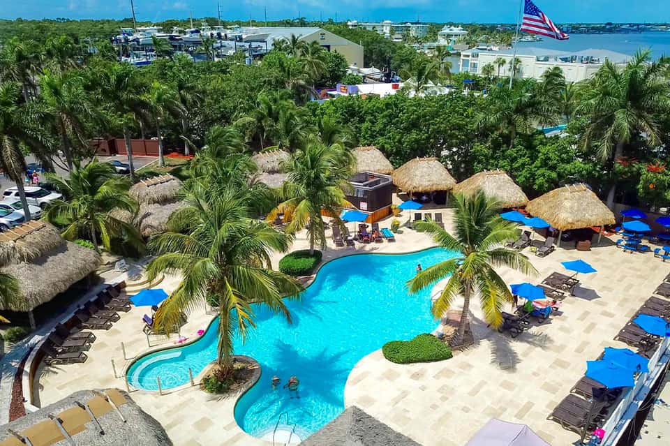 Aerial view of beachfront resort with turquoise pools, thatched umbrellas, palm trees, and waterfront