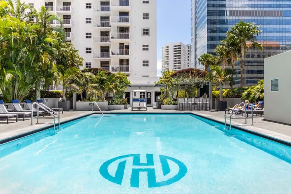 Resort swimming pool with branded logo, surrounded by palm trees and residential buildings