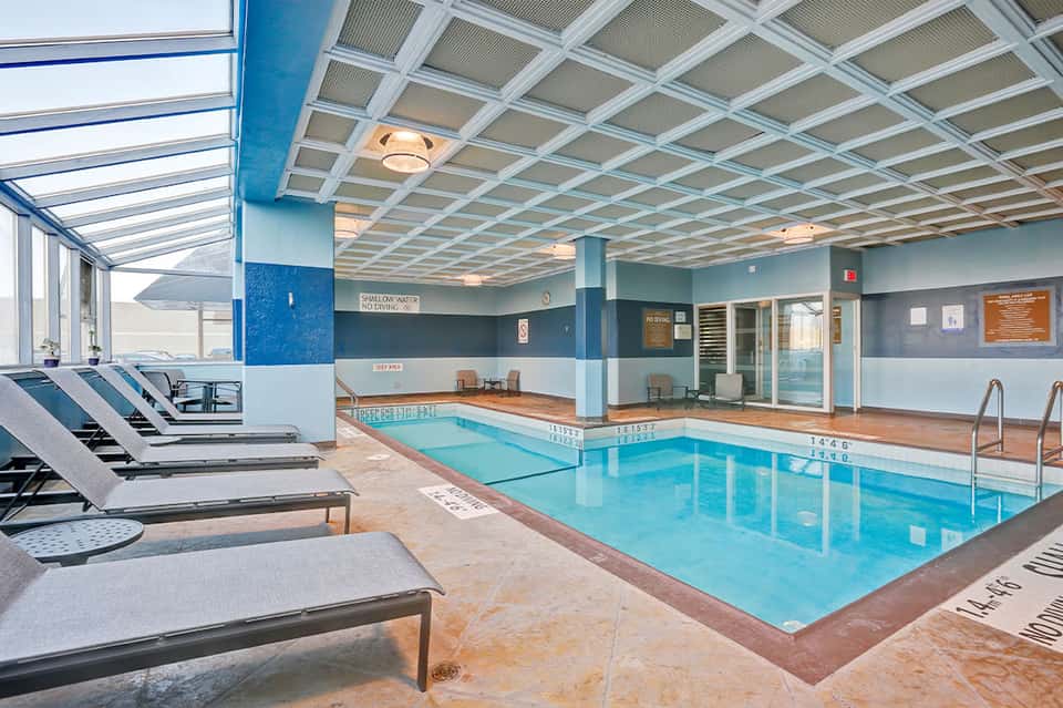Indoor heated pool with lounge chairs, skylights, and modern blue and white color scheme