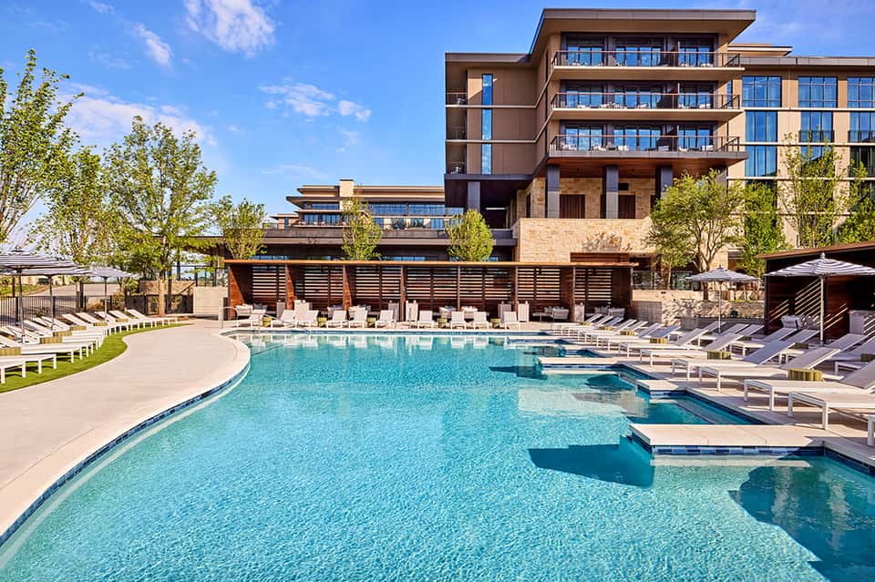Modern resort pool with lounge chairs, wooden pergola, and contemporary architecture