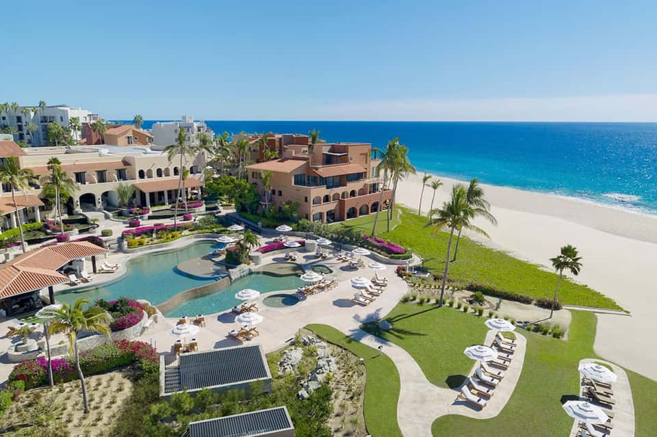 Aerial view of beachfront resort with pools, palm trees, and ocean views
