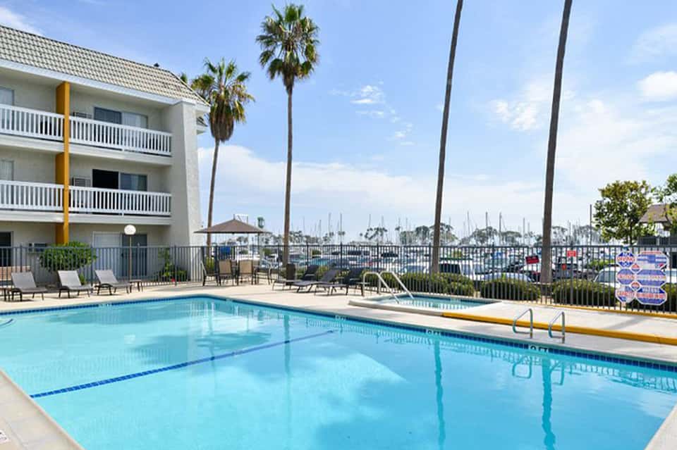 Resort pool with clear blue water, palm trees, modern building, and marina view in background